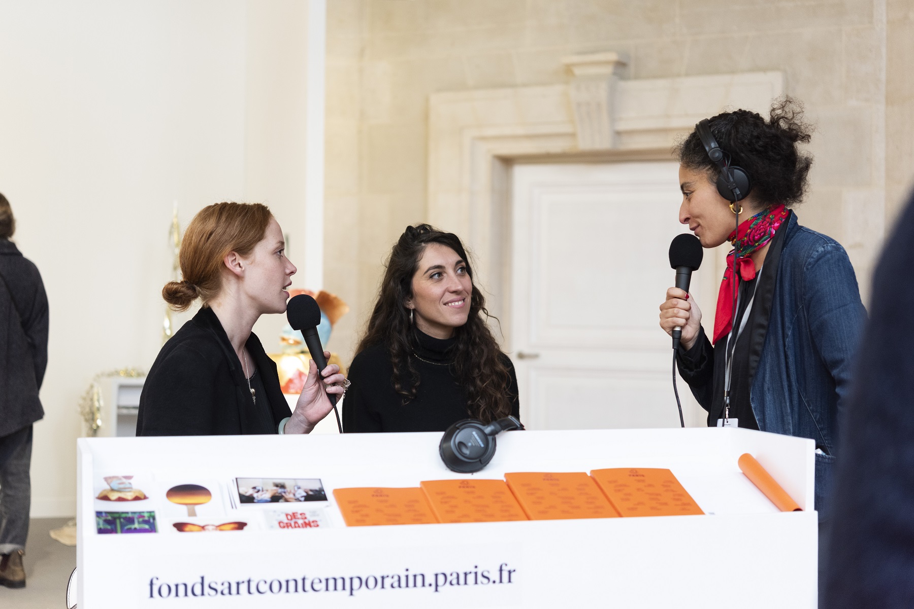 deux femmes assises et une femme debout parlent devant un micro