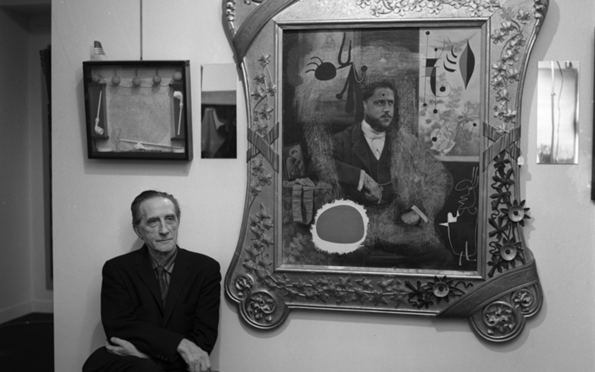 L'artiste Marcel Duchamp, décembre 1960, assis à côté d'une de ses oeuvres.