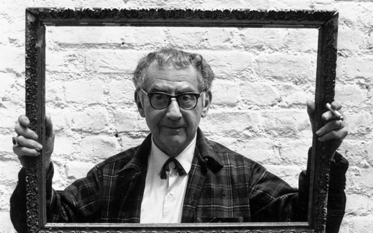 Le peintre, photographe et cinéaste Man Ray (1890 - 1976) regardant à travers un cadre qu'il tient en l'air alors qu'il se tient contre un mur blanchi à la chaux.