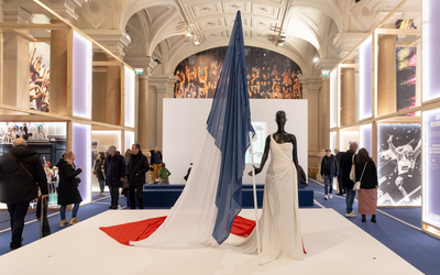 Dans une salle de l'Hôtel de Ville, une robe blanche drapée exposée signée Dior, avec un grand drapeau français tenu par le mannequin 