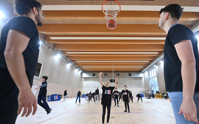 Une jeune fille s'entraine au tir au panier de basket sous le regard de deux entraineur de la NBA