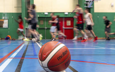 Personnes en arrière-plan s'entraînant dans un gymnase avec un ballon de basket au premier plan. 