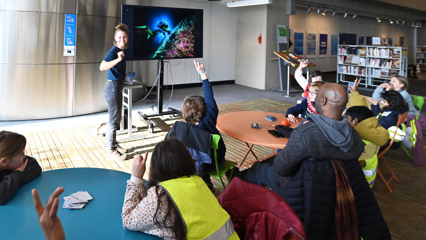 Les enfants  regardent des images de fonds sous marins projetés sur écran et interagissent avec une animatrice