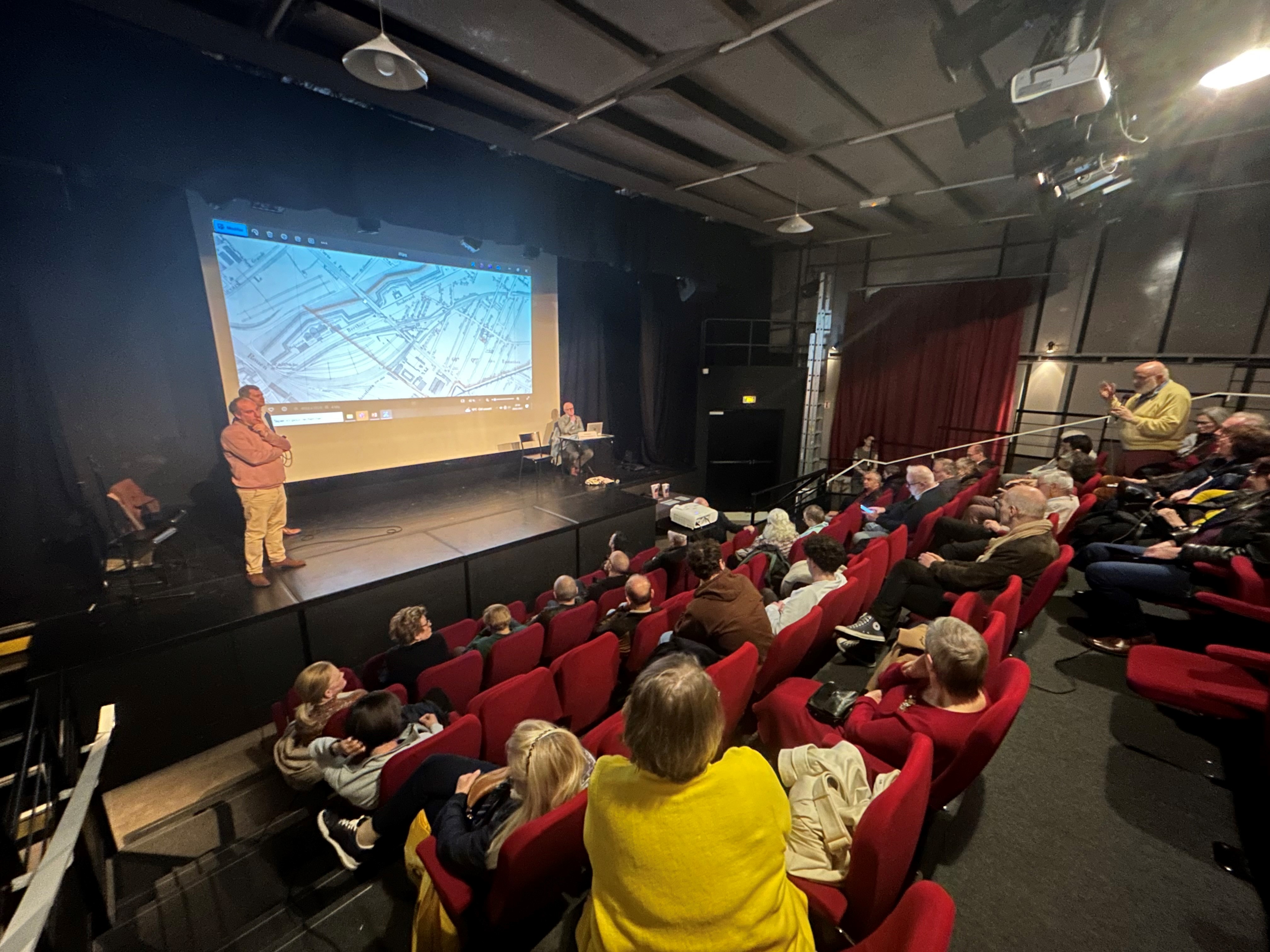 Photo de la réunion au sein de l'auditorium du centre paris anim la jonquière. La photo est prise d'en haut, permettant de voir le public et les intervenants se tenant debout sur scène