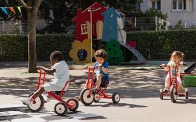 Trois enfants font du vélo en tricycles rouges dans une cour