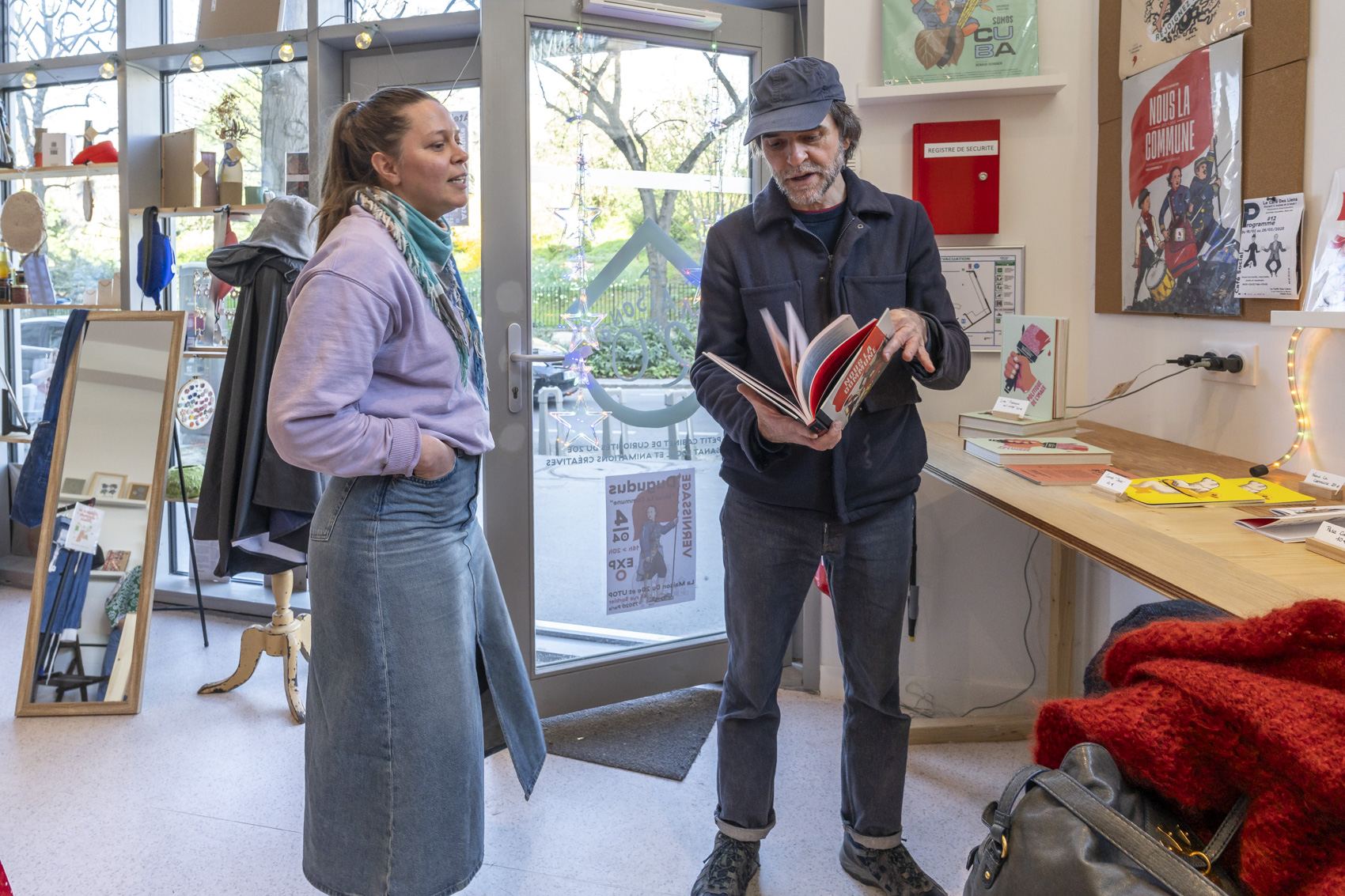Une jeune femme debout discute avec un homme qui feuillette un livre