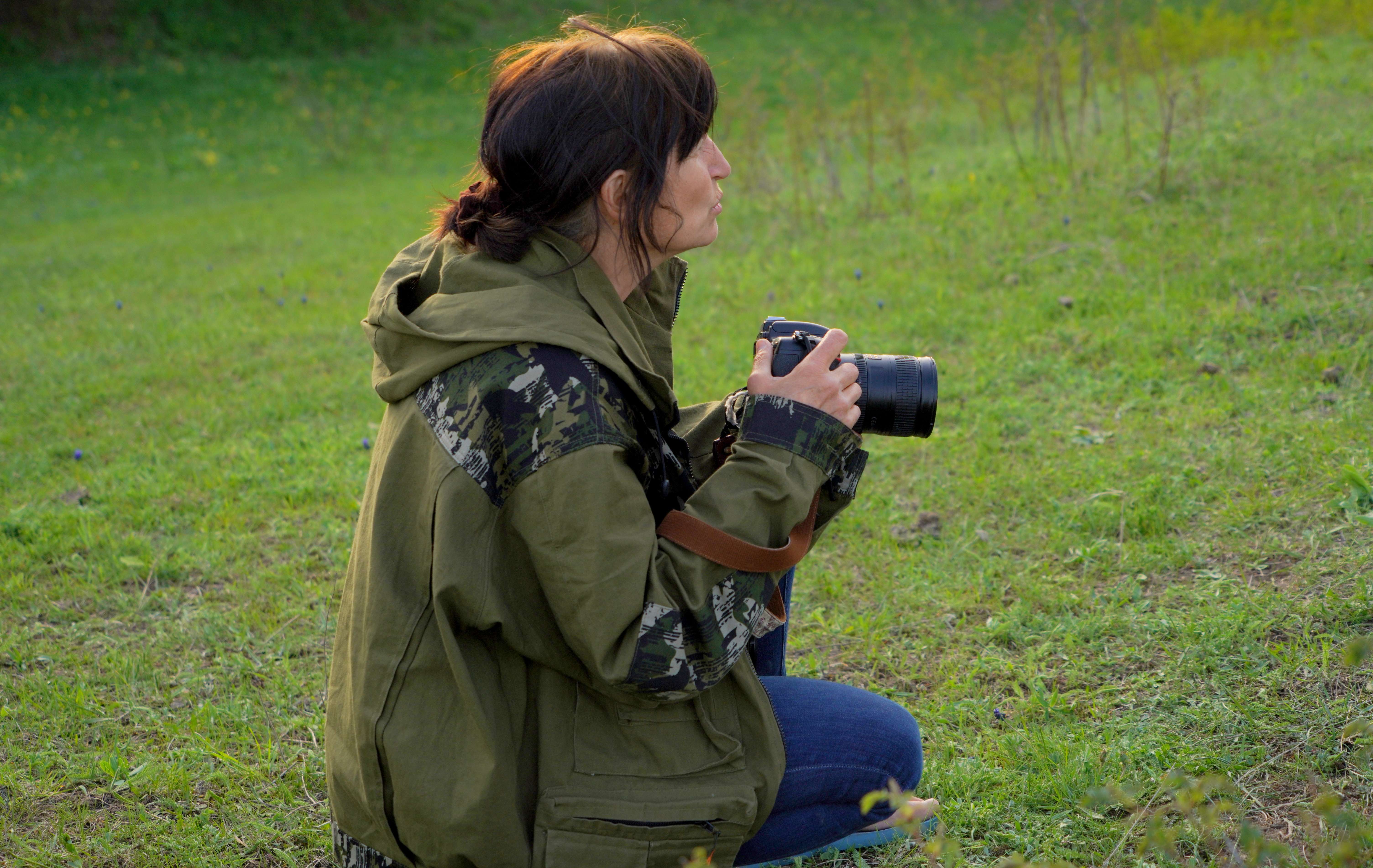 femme accroupie dans l'herbe, appareil photo à la main