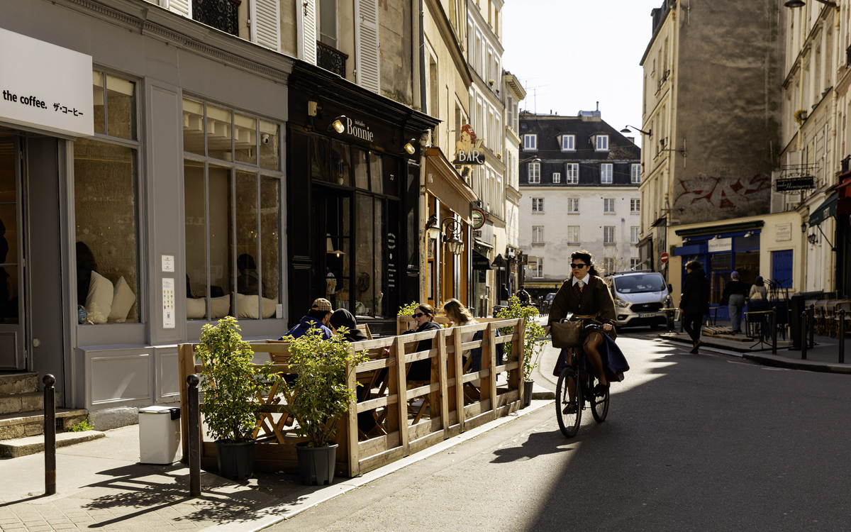 Une cycliste passe devant une terrasse estivale. 