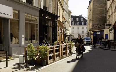 Une cycliste passe devant une terrasse estivale. 