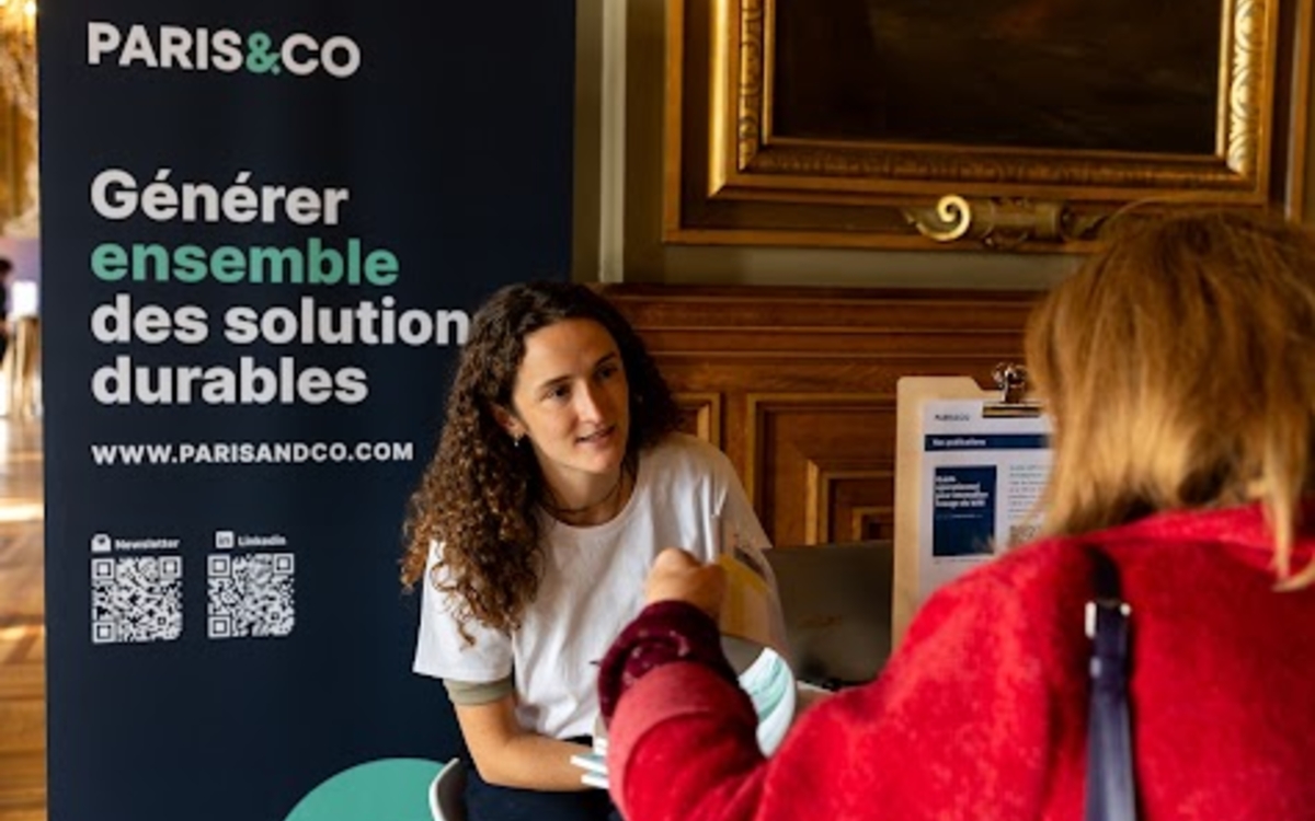 Un membre de l'équipe de Paris&Co échange avec une personne. Derrière, un kakemono de Paris&co avec le slogan " Générer ensemble des solutions durables