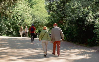 Deux personnes âgées se promènent sous le soleil des Buttes Chaumont. 