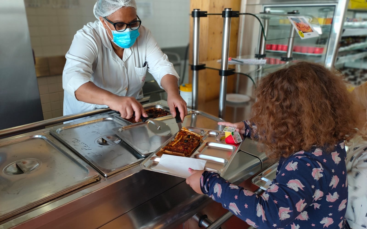 Une élève se faisant servir à manger dans son plateau en inox