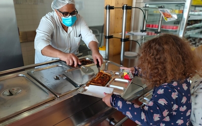 Une élève se faisant servir à manger dans son plateau en inox 