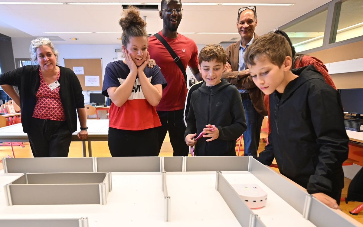 un petit groupe de collégiens accompagnés de leurs adjoints éducatifs observent leur robot parcours le chemin du labyrinthe jusqu'à la ligne d'arrivée