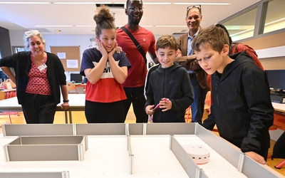 un petit groupe de collégiens accompagnés de leurs adjoints éducatifs observent leur robot parcours le chemin du labyrinthe jusqu'à la ligne d'arrivée