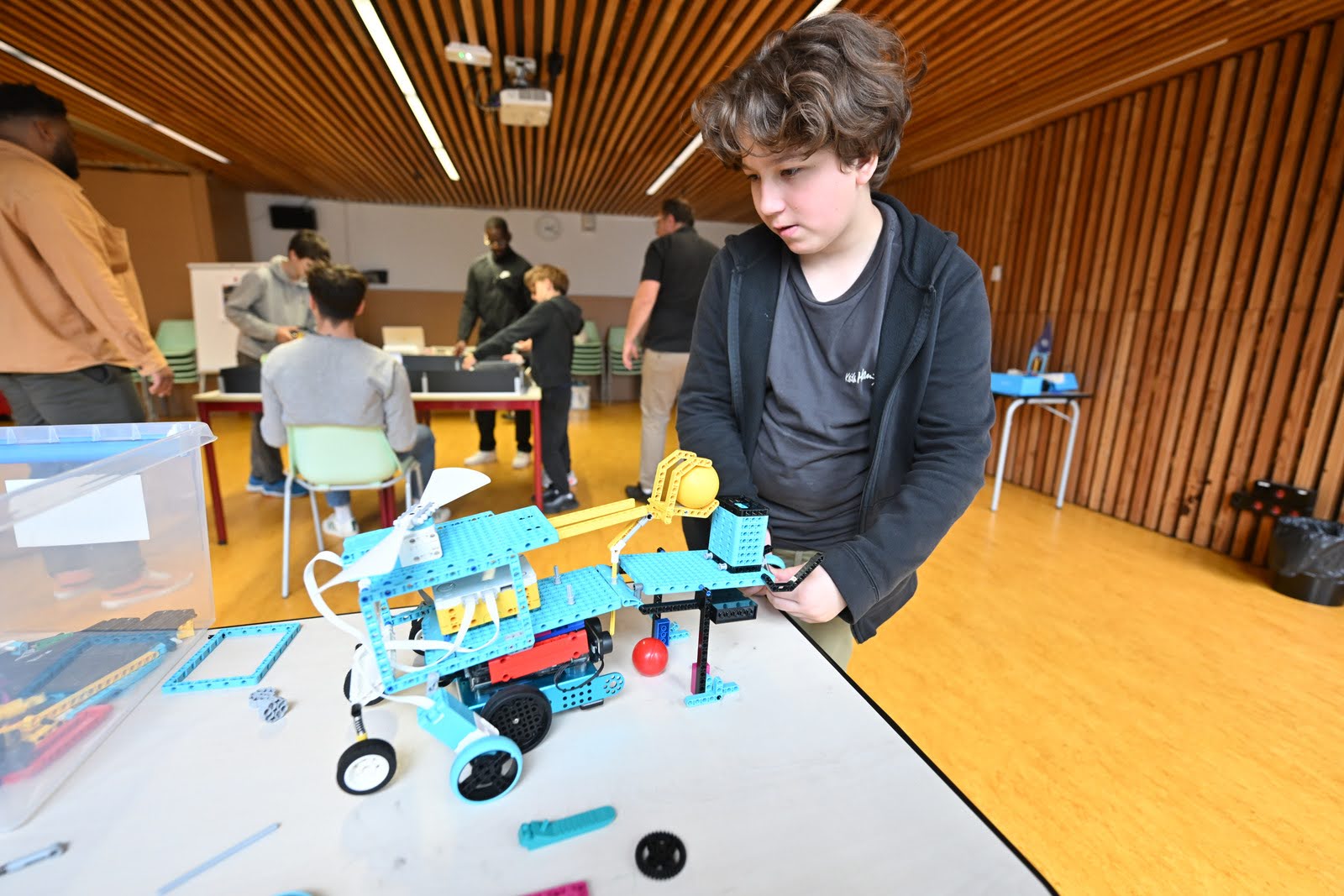 un collégien règle les derniers détails sur son robot agrémenté de Légo bleus et jaunes