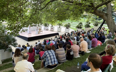 Des gesn rassemblés autour d'une scène de théâtre de verdure et assistant à une pièce en plein air