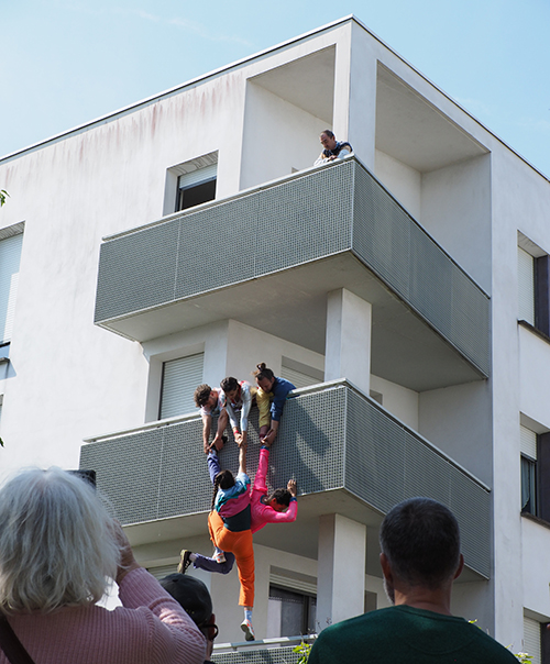 Cinq artistes suspendus aux façades, accrochés aux fenêtres, en équilibre sur les balcons