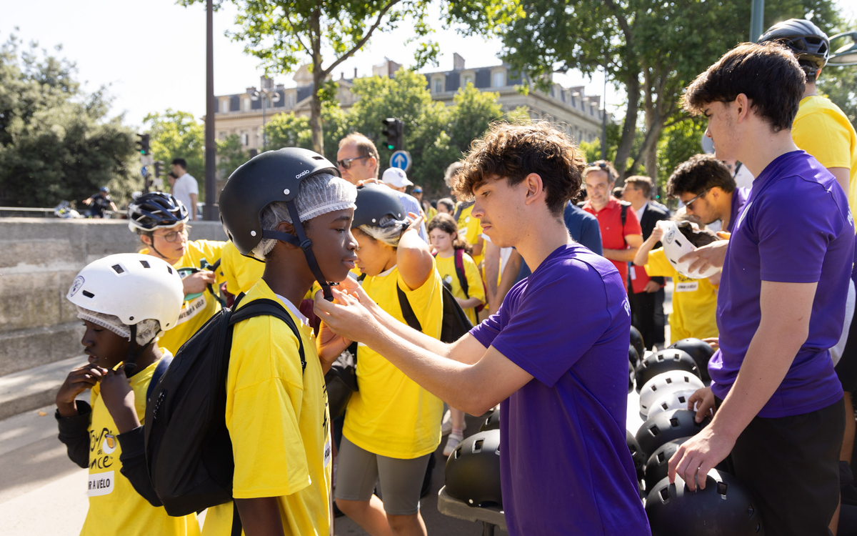 Un bénévole attache le casque de vélo d'un ado lors de la petite étape du tour. 