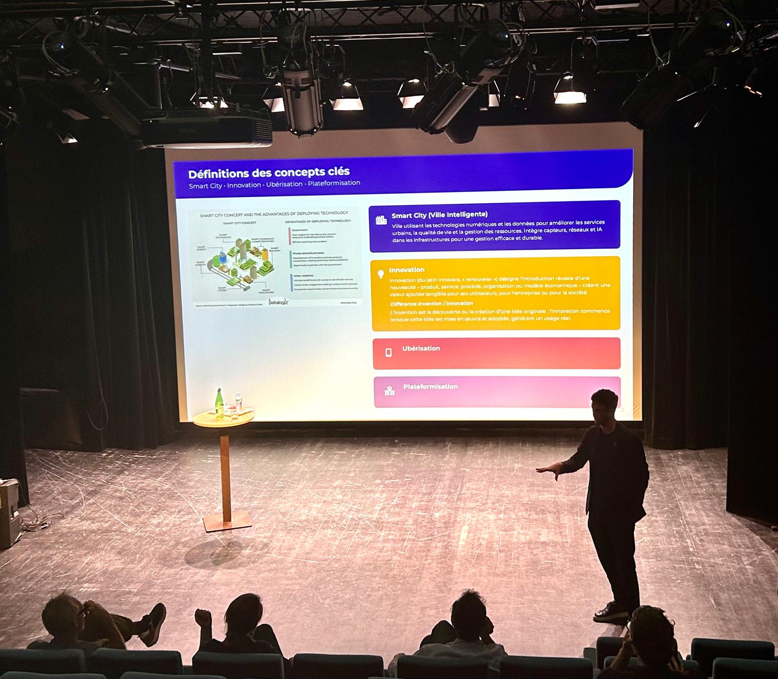 Réunion pblique dans un auditorium avec un homme sur scène et un grand écran
