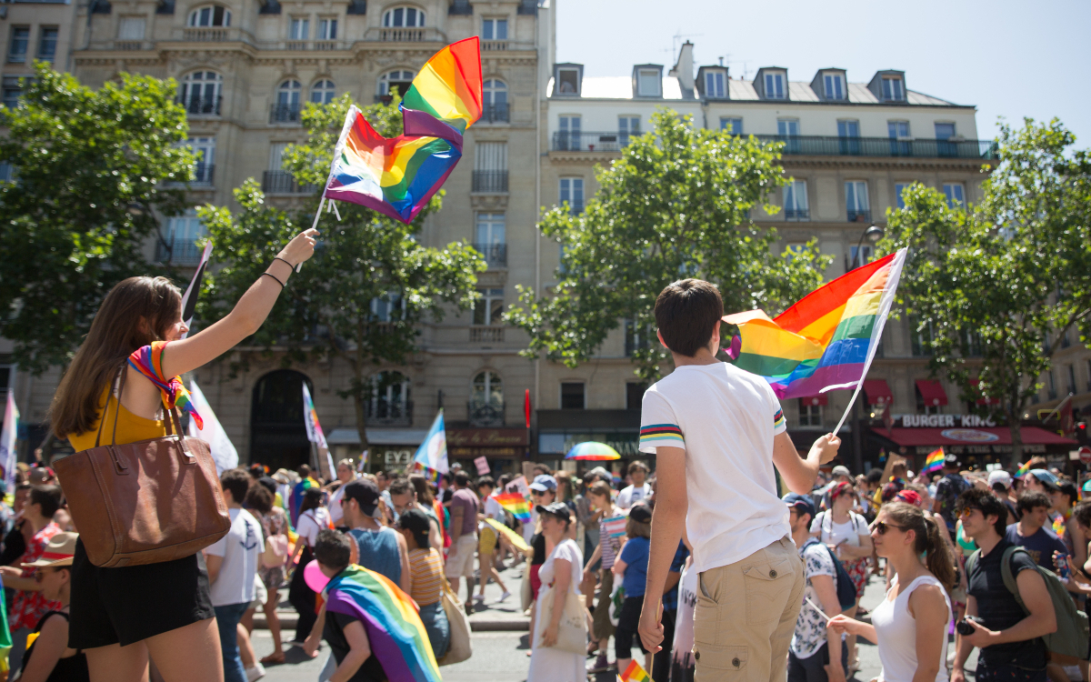 Deux personnes brandissant le drapeau LGBTQIA+ lors de la marche des fiertés.