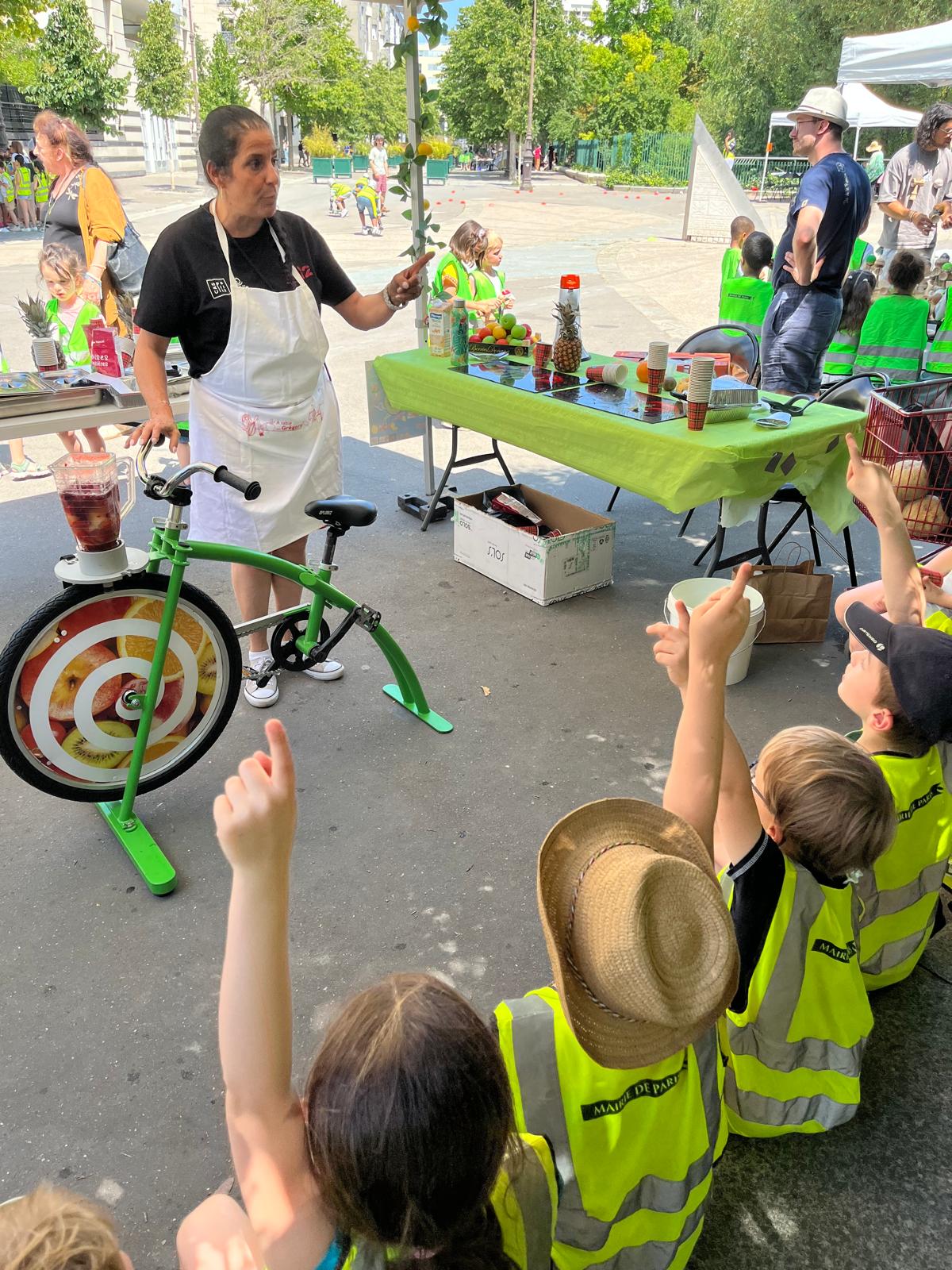 Un e animatrice fait une démonstration de vélo smoothie devant des enfants en gilets jaunes