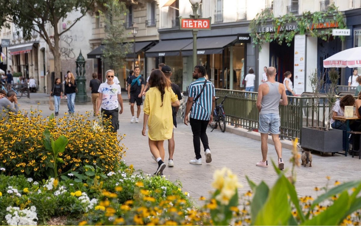 Photo de la place Albert-Memmi, au niveau de la sortie de métro Hôtel de Ville. Les jardinières et la végétation, sont au premier plan, on y voit des gens flâner et être installés en terrasse