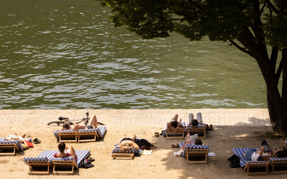 Des personnes se reposent sur des transat posés sur le sable de Paris Plages, en bordure de Seine.