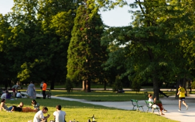 Des gens se prélassent sur une pelouse, regardant des gens courir et le Bois de Vincennes en arrière plan