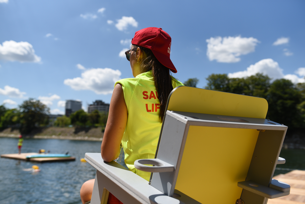 Habillée d'une casquette rouge et d'un tee shirt jaune fluo, une sauveteuse observe le bassin de nage du site de baignade de Grenelle.