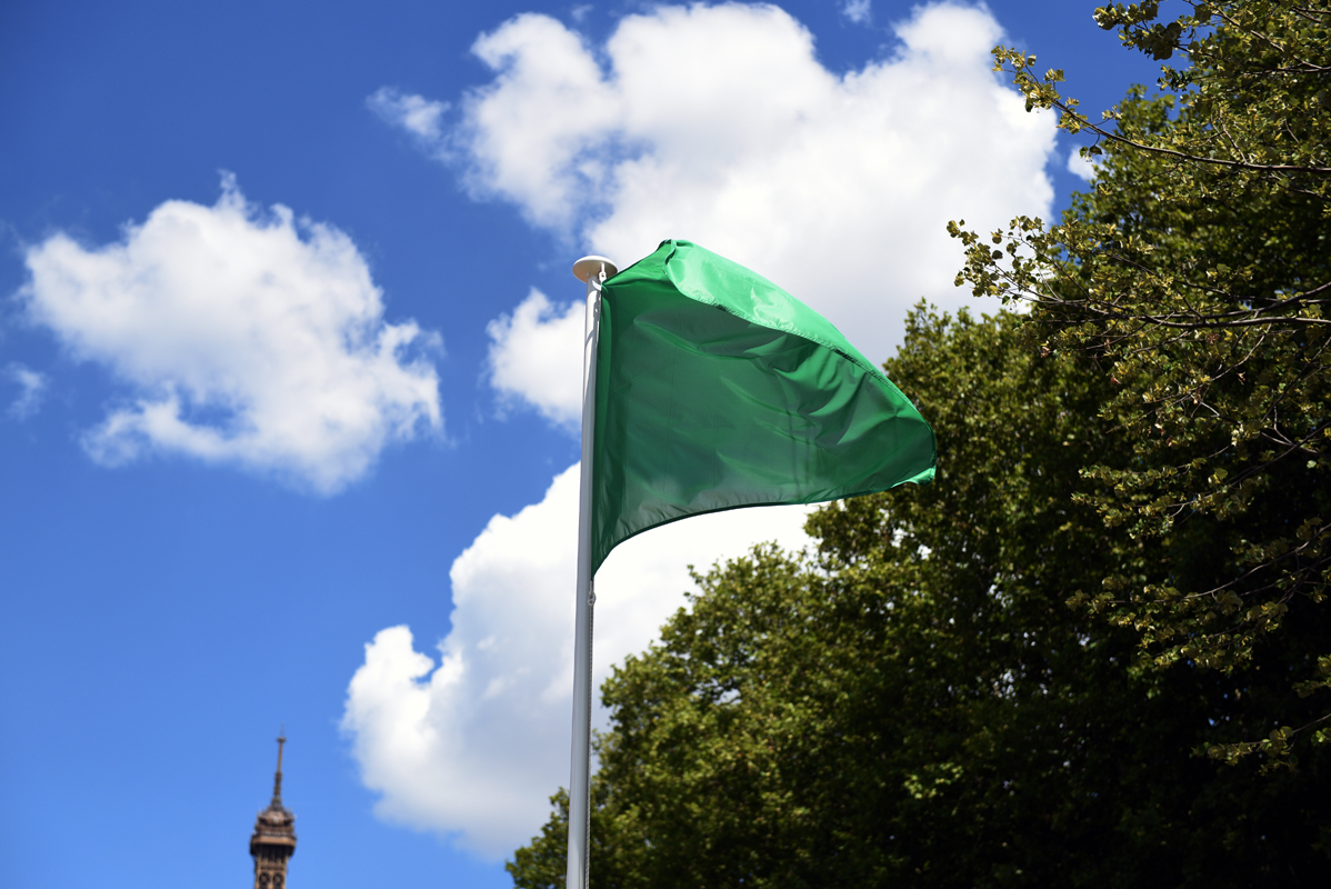 Du site de baignade de Grenelle, on peut voir un drapeau vert flotté dans les airs et tour Eiffel en arrière plan.
