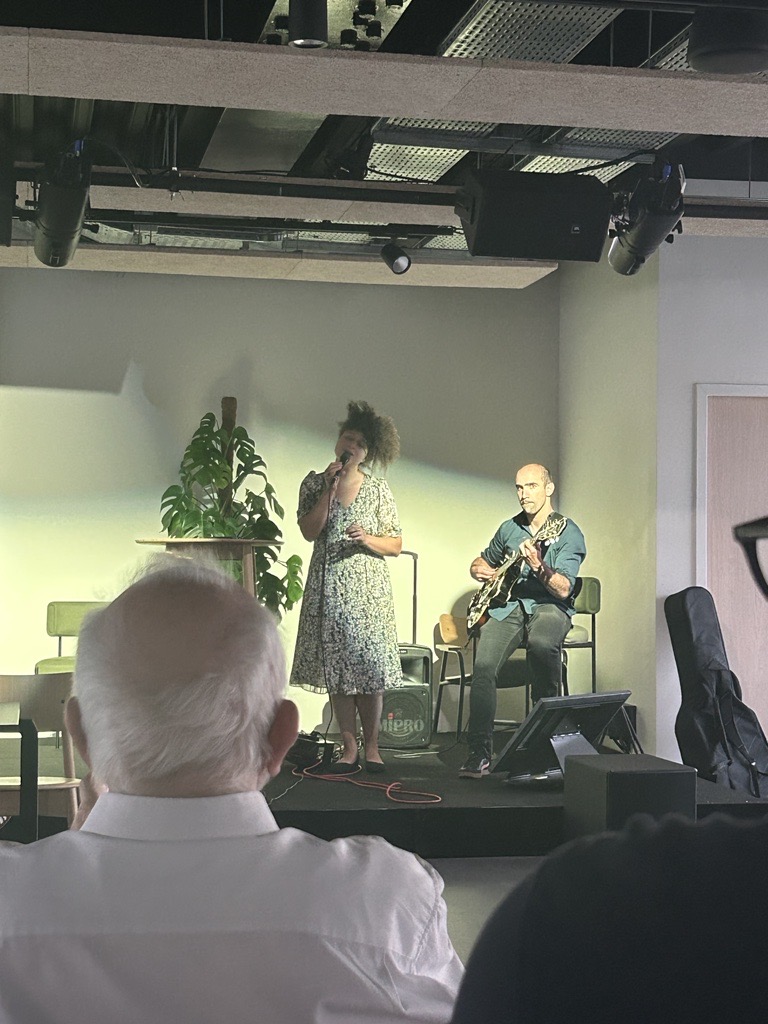 Vue depuis le fond de la salle sur la chanteuse Chloé Cassandre en pleine prestation. On voit également le guitariste assis à côté d'elle en train de jouer