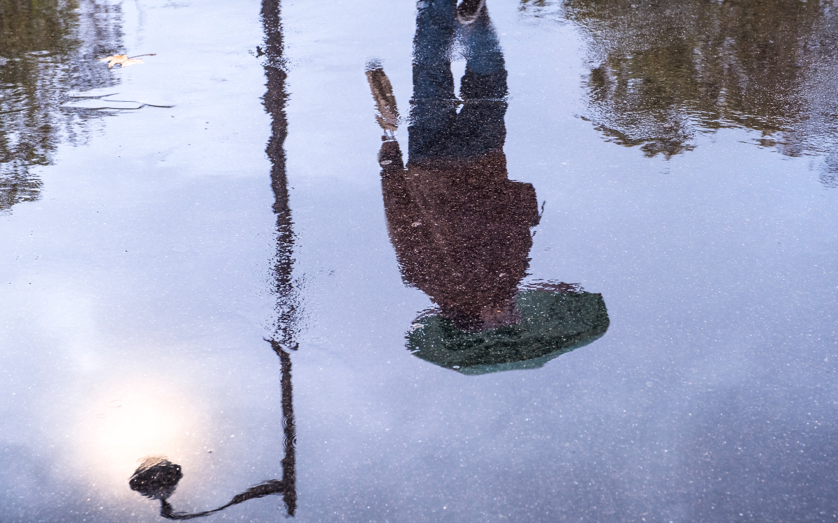 Silhouette d'une personne portant un parapluie sur le sol mouillé. 