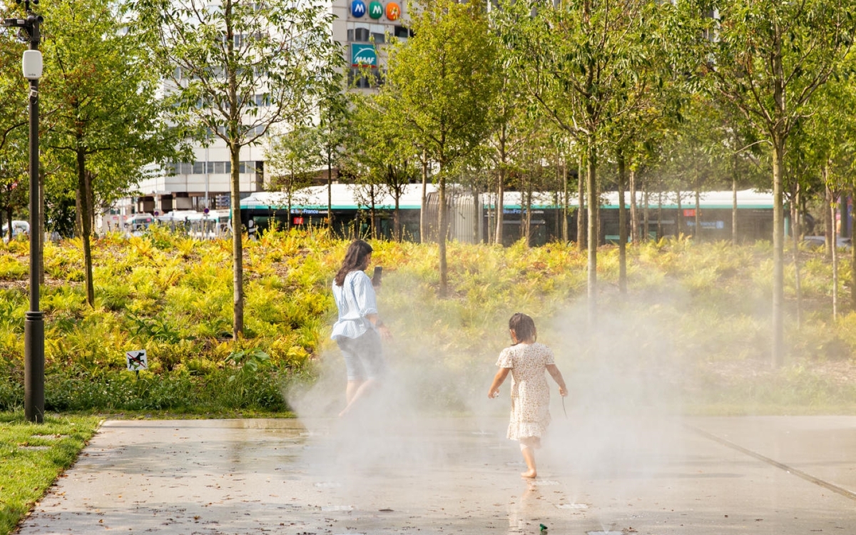 Enfants jouant avec l'eau des brumisateurs au sol dans la forêt urbaine sur la place
