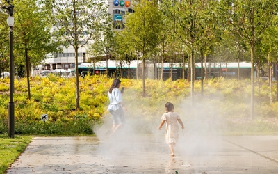 Enfants jouant avec l'eau des brumisateurs au sol dans la forêt urbaine sur la place