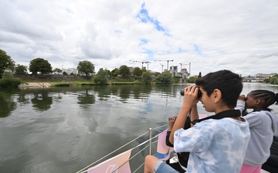 Deux adolescents sur un bateau observent les berges de la Seine avec des jumelles