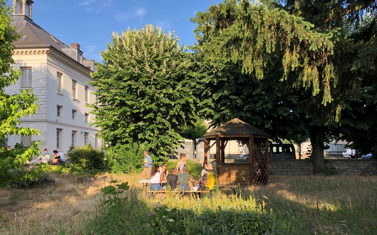 Groupe de jeunes gens profitant sur soleil à la tombée de la journée entouré par la nature avec le bâtiment de l'ancien hôpital en fond