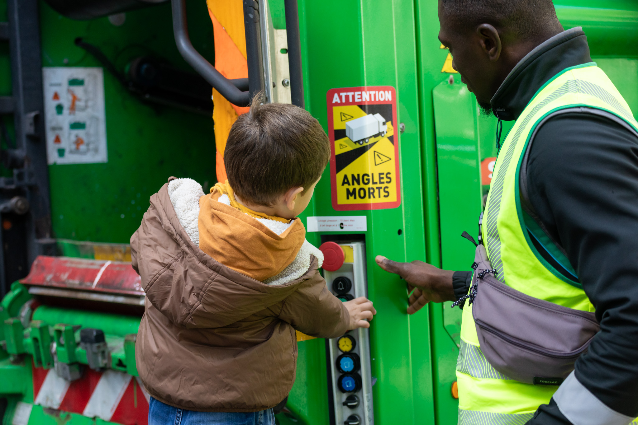 Un enfant à l'arrière d'un camion benne, sous le regard d'un agent de la propreté