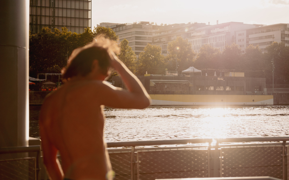 Une personne floutée en premier plan devant le reflet du soleil sur la baignade à Bercy en Septembre 