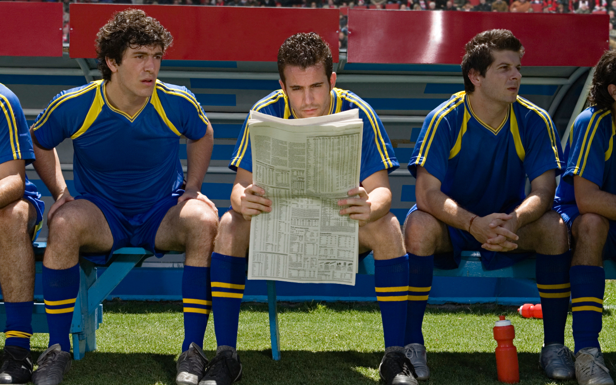 Un footballeur lisant le journal sur le banc de touche.
