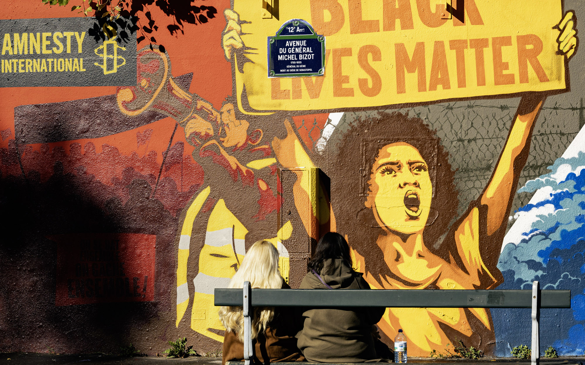 Deux personnes assises sur un banc devant la nouvelle fresque du mur des droits humains par l'artiste RNST (12e) 