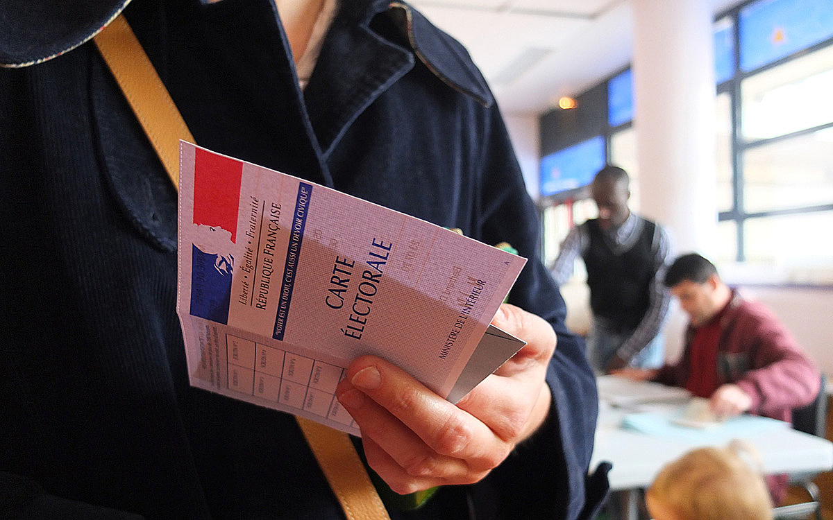 personne dans un bureau de vote avec carte électorale à la main