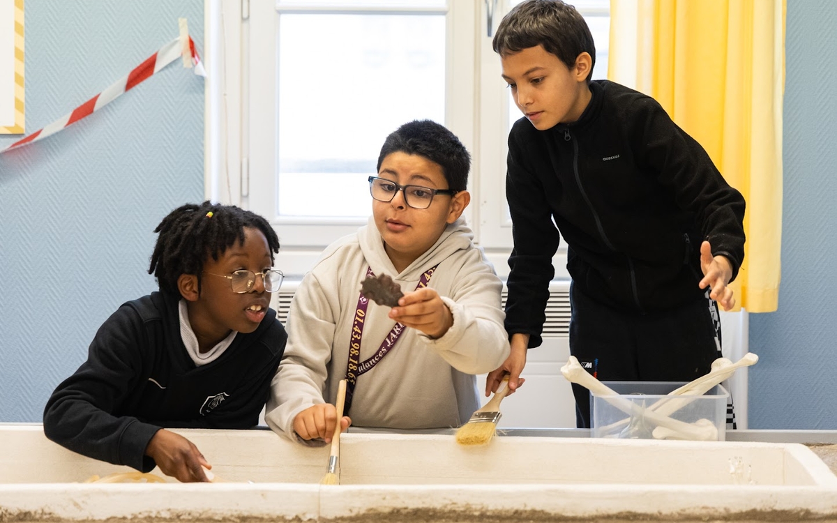 Enfants observant un objet découvert dans une sépulture mérovingienne reconstituée lors d’un atelier archéologique.