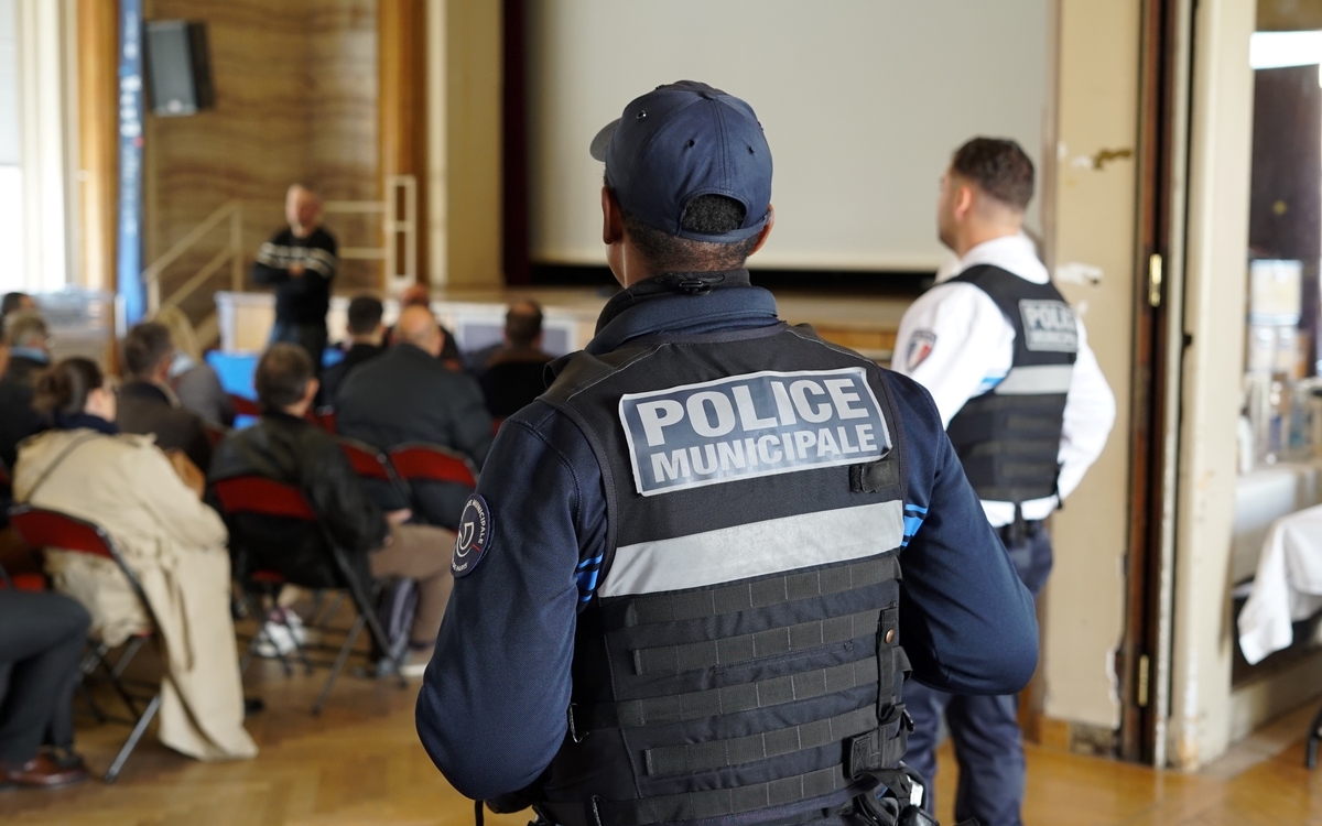 Policier municipal de dos avec foule assise au second plan 
