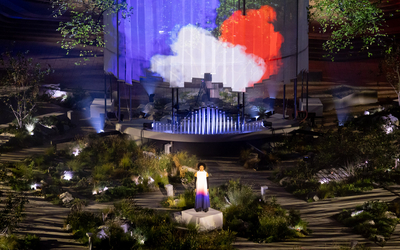 Chanteuse au jardin mémoriel devant un drapeau tricolore projeté.