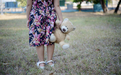 Une enfant seule dans un jardin avec un nounours à la main.