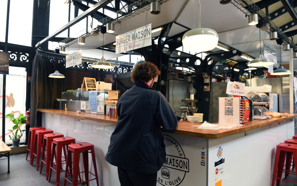 Un client au stand burger du marché couvert de la Chapelle, dit marché de l'Olive,  18e.