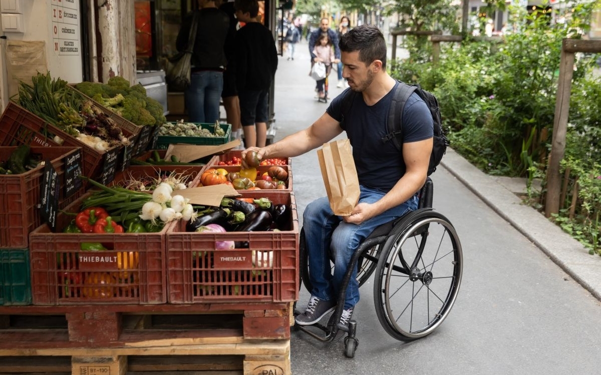 homme en fauteuil roulant en train de choisir des légumes à un étal