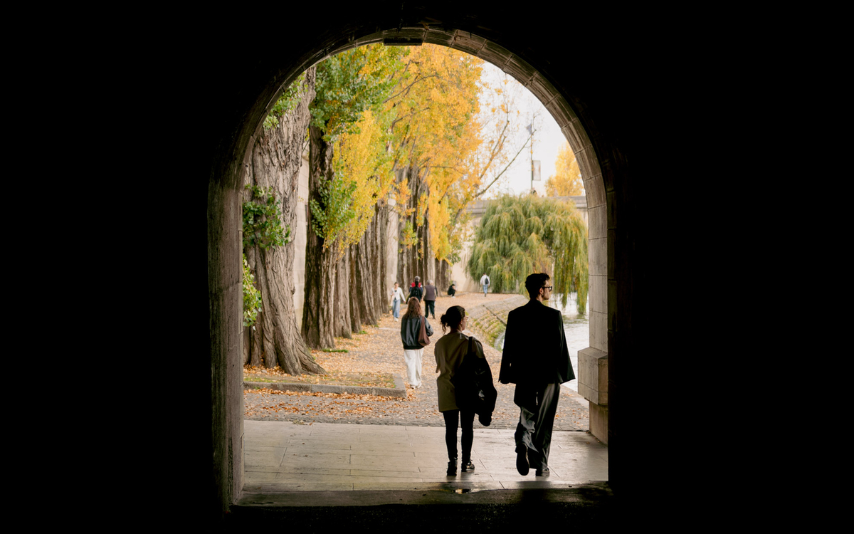 Deux personnes se promènent sur la promenade Marceline-Loridan-Ivens, sous le pont du Carrousel.