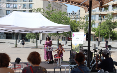 Une chanteuse et une violoncelliste proposent une représentation à des passants et habitants installés sous une ombrière sur la voie publique